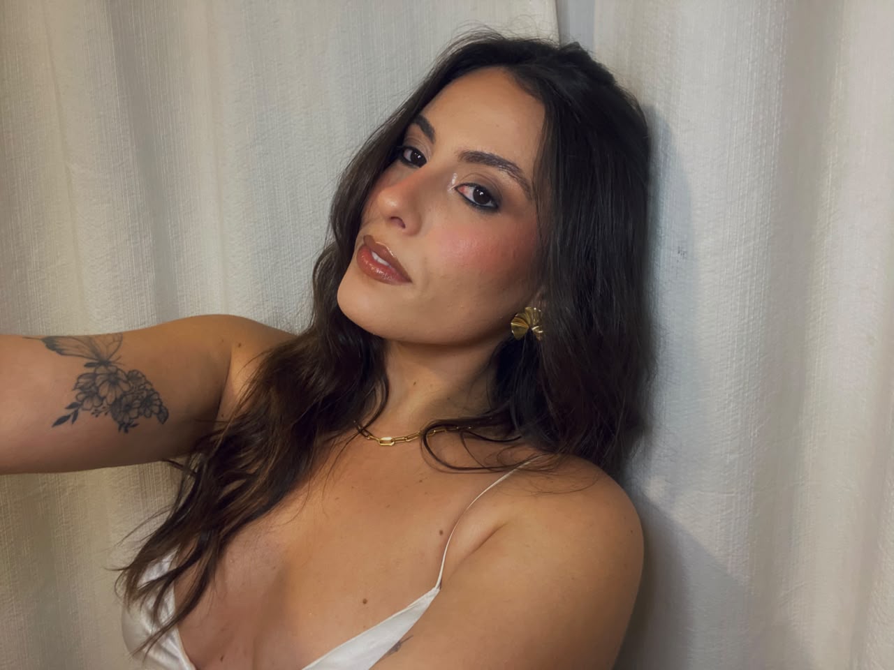 Bettina Poll em selfie com brinco dourado e blusa de cetim clara